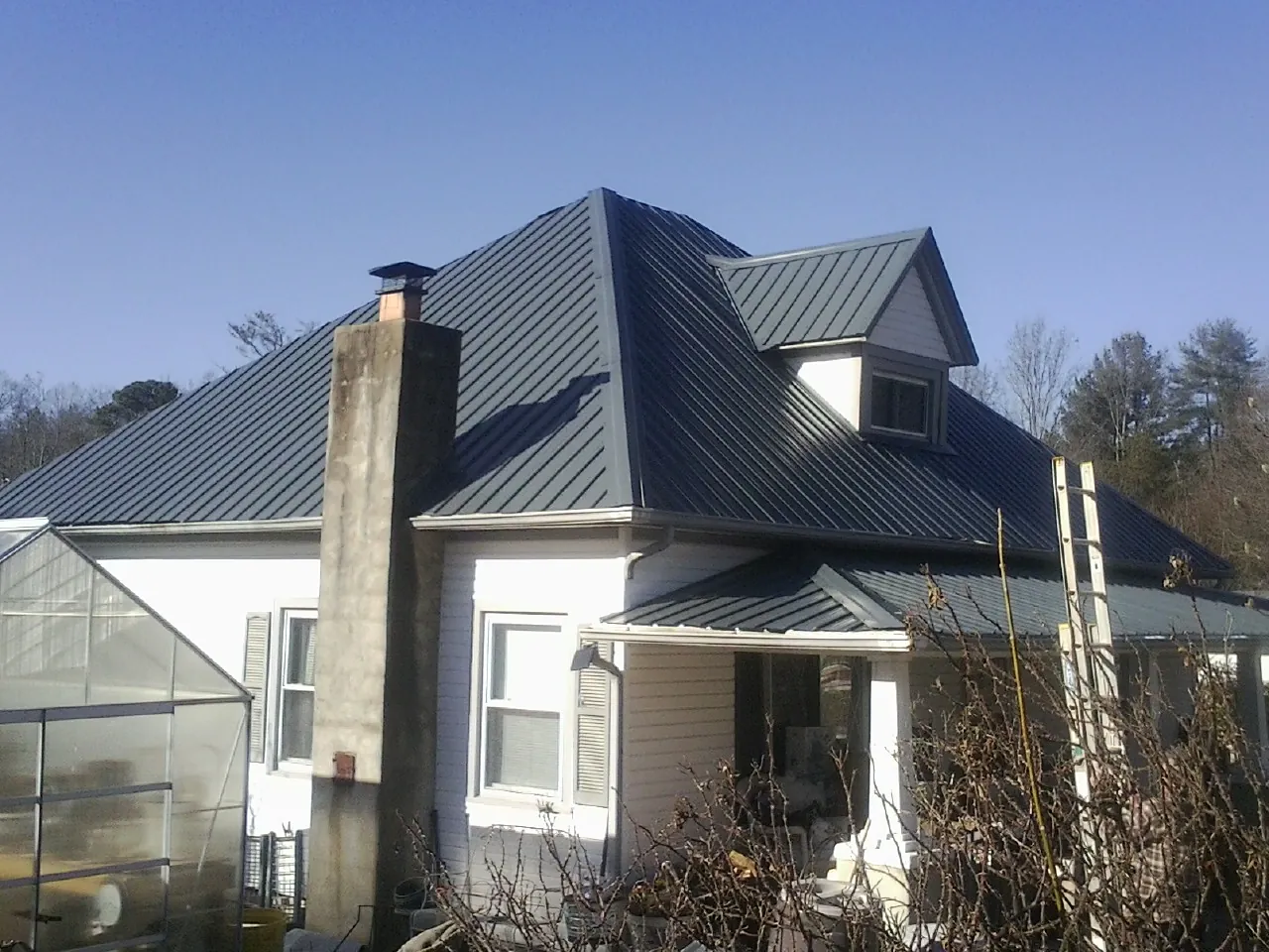 Dark blue standing seam metal roof on a white farmhouse with dormer — Slate & Tile Roof Repair by Roofing Brothers in Mason City