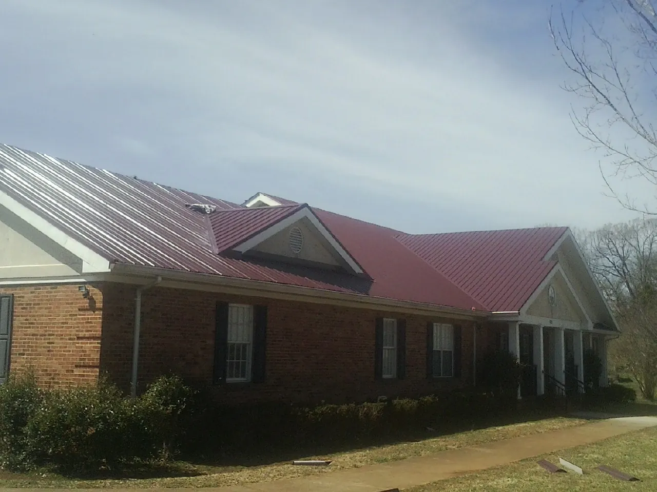Red metal roof with gabled entries on a long brick building, from a Hail Damage Roof Repair job in Mason City