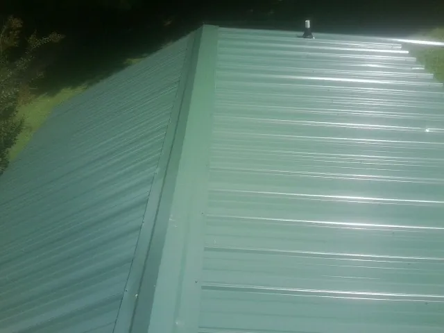 New green metal panels meeting at the ridge of a roof — Flat Roof Repair work by our crew in Mason City