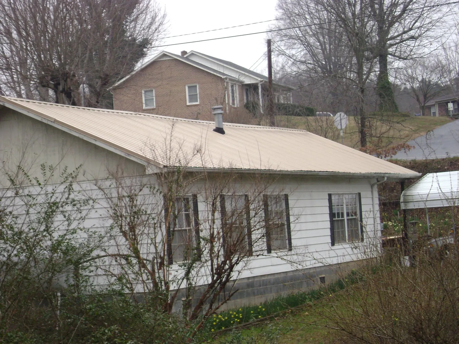 Tan metal roof on a white sided house set into a hillside — Commercial Roofing by Roofing Brothers in Mason City