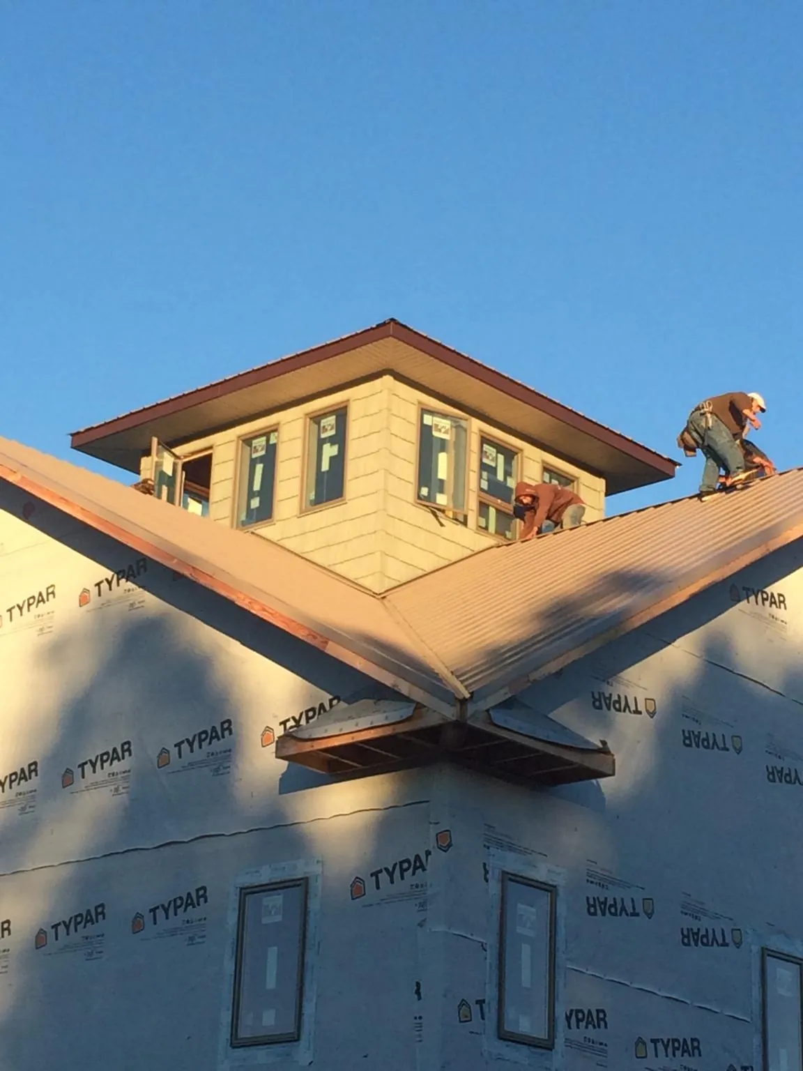 Roofers working around a rooftop cupola on a new metal roof at sunset — Roof Waterproofing in Mason City by Roofing Brothers